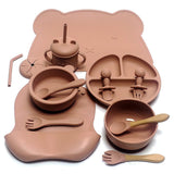 Ensemble repas complet en silicone – Édition Ourson, comprenant 10 pièces en silicone sans BPA : assiette compartimentée, bols, gobelet à paille, couverts bois‑silicone et tapis en forme d’ourson, le tout dans une teinte douce et chaleureuse.